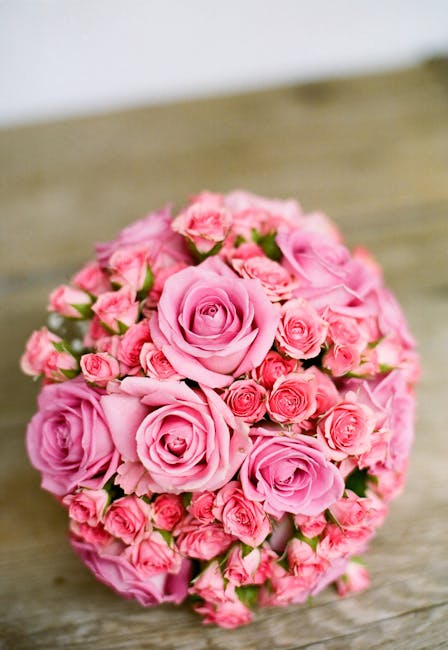 A bouquet arrangement of fresh pink roses and mini pink spray roses, densely packed and forming a rounded, floral gift. The roses vary in shades from soft blush to deeper pink, with velvety petals tha