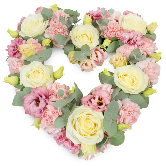 A richly detailed, heart-shaped wreath of pastel flowers appears on a crisp white background, the kind of refined funeral tribute you might see arriving at a chapel service near Wood Green station. The heart is flawlessly formed, its contours softened by layers of petals and foliage so that it feels both defined and gentle. Dominating the arrangement are cream and pale lemon-yellow roses, each bloom full and velvety, their petals curled in neat spirals that suggest devotion, gratitude, and quiet remembrance. Between these roses, clusters of light pink carnations create pockets of texture; their ruffled, many-layered petals lend a soft, almost billowing effect, like small clouds resting along the outline of the heart. Adding depth and richness, mauve and deep pink lisianthus blooms are interspersed throughout. Their more open, cup-shaped flowers and subtle tonal variations bring a graceful, romantic quality, guiding the eye from one side of the heart to the other. Small yellow-green buds punctuate the design, promising new growth and offering a gentle contrast to the pastels. Threaded throughout, silvery-green eucalyptus leaves with round and oval shapes create cool accents and natural structure, framing the flowers with a calm, contemporary touch. The composition is dense and luxurious, yet the colour harmony maintains a soothing, peaceful feeling, making it well-suited for funerals, memorial services, or anniversary remembrances across Wood Green and the wider N22 community. This floral heart feels like a silent message of compassion and presence for families gathering to say goodbye.